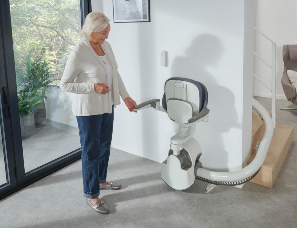 An older woman checking the flow X stairlifts arms for an emergency call button